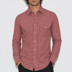 May include: A red and white plaid button-down shirt with a chest pocket. The long-sleeved shirt is made of a lightweight fabric and has a classic collar. The shirt is buttoned up and is worn by a person.