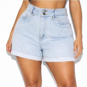 May include: Light blue denim shorts with a high waist and rolled cuffs. The shorts have two front pockets and a double-button closure. The denim is a light wash, giving them a casual, everyday look.