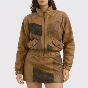 May include: A brown leather jacket and matching skirt set. The jacket has a high collar, a zipper closure, and two front pockets. The skirt is a mini skirt with a high waist. The set is made of patchwork leather in various shades of brown.