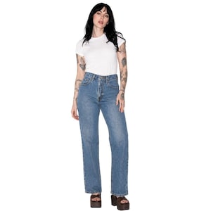 May include: A woman wearing a white crew neck t-shirt and light blue denim jeans. The jeans have a high waist and a straight leg fit. The woman is wearing brown platform sandals.