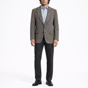 May include: A brown tweed blazer with a two-button closure, paired with a light blue dress shirt and dark gray trousers. The outfit is completed with black leather dress shoes, creating a classic, tailored look.
