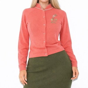 May include: Coral-colored cardigan with a round neckline and long sleeves. The button-down sweater features a small floral embroidery on the left chest. The collar and button placket are trimmed with a thin white piping.