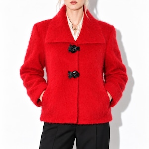 May include: A bright red fuzzy textured jacket with a wide collar and two black decorative toggle closures on the front. The jacket is worn over a white collared shirt and is paired with black trousers, creating a bold and vibrant look.