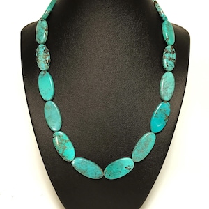 May include: A necklace featuring a series of smooth, oval-shaped turquoise beads. Each bead displays a vibrant cyan blue color with natural dark brown matrix veining throughout. The beads are arranged in a single strand, gradually increasing in size toward the center of the necklace, creating a uniform and balanced appearance.