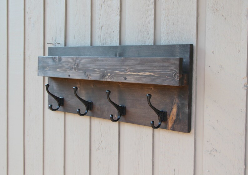 May include: A dark brown wooden wall mounted shelf with a small shelf on top and four black metal hooks underneath.