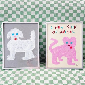 May include: Two framed illustrations of cartoon animals. The left frame shows a white dog with blue eyes and a red mouth on a gray background. The right frame shows a pink cat with blue eyes and a red nose on a white background. The text "A NEW KIND OF ANIMAL" is written in red, blue, and black letters above the cat.