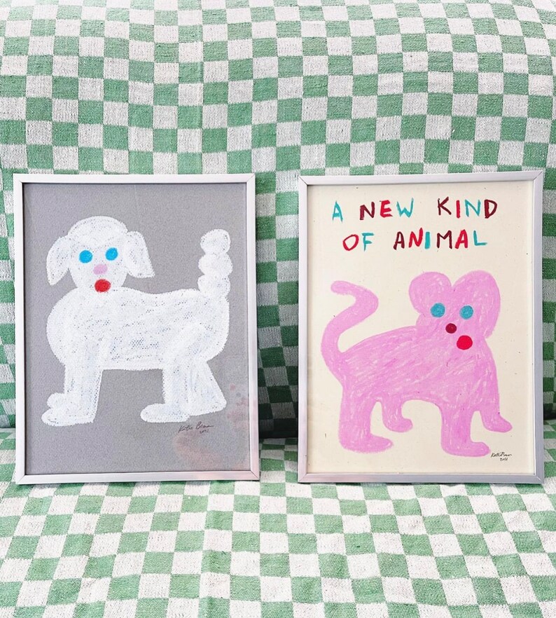 May include: Two framed illustrations of cartoon animals. The left frame shows a white dog with blue eyes and a red mouth on a gray background. The right frame shows a pink cat with blue eyes and a red nose on a white background. The text "A NEW KIND OF ANIMAL" is written in red, blue, and black letters above the cat.