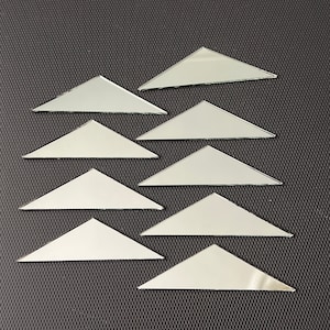 May include: A set of eight silver triangular mirror tiles arranged in a staggered pattern on a black textured surface.