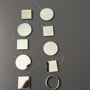 May include: A set of silver-colored mirror tiles in various shapes, including circles and squares, strung together with white thread. A silver ring is also included.
