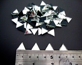 May include: A collection of small, mirrored triangle tiles, some with black backing, scattered on a dark surface. A ruler with inch and millimeter markings is at the bottom, showing the size of the tiles. These tiles could be used for mosaic art or crafts.