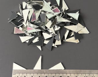 May include: A pile of small, triangular mosaic tiles in black, white, and mirrored silver. A ruler shows the tiles are approximately 1 inch to 1.5 inches in length. The tiles are scattered on a gray surface.