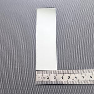Op de afbeelding: Een wit, rechthoekig object ligt naast een metalen liniaal. De liniaal toont metingen in centimeters, waarbij de lengte van het object ongeveer 3 cm is. De achtergrond is een gestructureerd grijs oppervlak.