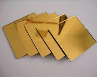 May include: A collection of five square, gold-colored mirrored tiles arranged in a slightly overlapping pattern. The tiles have a reflective surface, and the edges appear to be beveled. The overall effect is a modern, minimalist aesthetic.