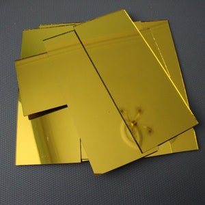 Puede incluir: Un conjunto de azulejos de espejo dorados. Los azulejos son rectangulares y tienen una superficie lisa y reflectante.