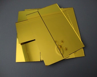 May include: A stack of gold mirror tiles. The tiles are rectangular and have a smooth, reflective surface.