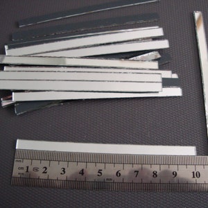 May include: A pile of silver mirror tiles, some with black backing, next to a ruler marked in centimetres and inches. The ruler measures 12 centimetres or 4.7 inches.