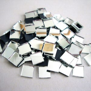 Può includere: Un mucchio di piccole piastrelle quadrate di vetro a specchio. Le piastrelle sono argentate e riflettono la luce, con alcune piastrelle nere mescolate. Queste tessere di mosaico sono adatte a vari progetti artigianali.