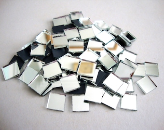 May include: A pile of small, square, mirrored glass tiles. The tiles are silver and reflect light, with some black tiles mixed in. These mosaic tiles are suitable for various craft projects.