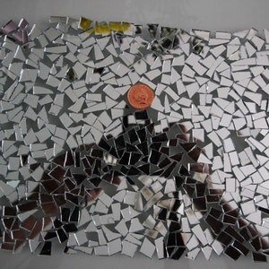 Könnte beinhalten: Eine große Sammlung kleiner, unregelmäßiger, silberfarbener Spiegelkacheln. Die Kacheln sind in einem zufälligen Muster angeordnet und erzeugen einen Mosaik-Effekt. Eine einzelne kupferfarbene Münze befindet sich in der Mitte des Mosaiks.