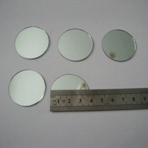 Puede incluir: Seis pequeños espejos redondos y reflectantes de vidrio están dispuestos sobre una superficie clara. Una regla metálica con marcas de centímetros se coloca cerca de los espejos. Los espejos tienen aproximadamente 2,5 cm de diámetro.