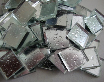 May include: A pile of small, square, silver-colored mirror tiles with a textured surface. The tiles are wet and have water droplets on them.