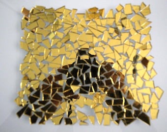 May include: A square arrangement of small, reflective gold-colored mirror shards. The pieces are irregularly shaped and vary in size, creating a mosaic-like pattern with gaps between each individual fragment, resulting in a textured, metallic surface.