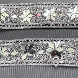 May include: Two strips of silver decorative trim. Each strip features a central band of small, sparkling rhinestones and mirrored star-shaped accents. The edges are finished with a delicate, openwork design.