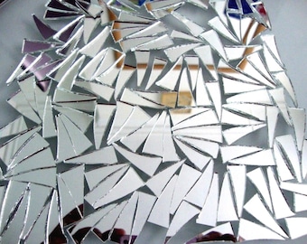 May include: A collection of small, triangular pieces of mirror glass, arranged in a random pattern. The pieces are all different sizes and shapes, and they reflect light in a variety of ways.