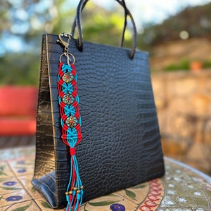 May include: A black leather tote bag with a blue and red tassel keychain. The keychain has a beaded tassel and a metal charm with a turquoise design.