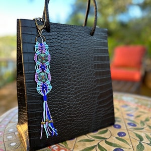 May include: A black crocodile embossed handbag with a blue, pink, and green beaded tassel keychain. The keychain features a butterfly design.