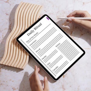 May include: A digital tablet displaying a "Daily Ritual" template with sections for the day, intention, ritual, herbs, oils, candle, and notes. The tablet is held near a wooden decorative piece. A stylus hovers above the screen.