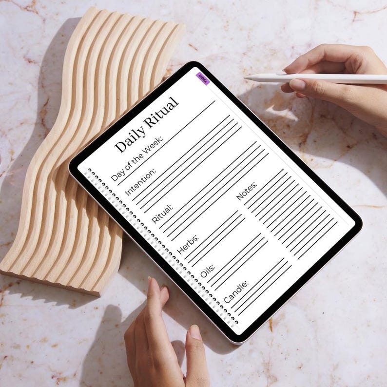 May include: A digital tablet displaying a "Daily Ritual" template with sections for the day, intention, ritual, herbs, oils, candle, and notes. The tablet is held near a wooden decorative piece. A stylus hovers above the screen.