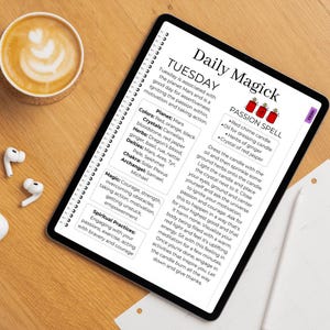 May include: A digital tablet displays a "Daily Magick" page with text about Tuesday, Mars, and a passion spell. The page includes a list of colors, crystals, herbs, deities, and a chakra. A cup of coffee and wireless earbuds are on the wooden surface.