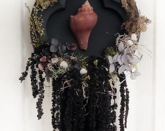 Spookachtige wanddecoratie aan zee met een zeeheks, echte gedroogde bloemen, kristallen en een op de kust geïnspireerde natuurlijke kunstkrans van kristallen en een heksendecoratie.