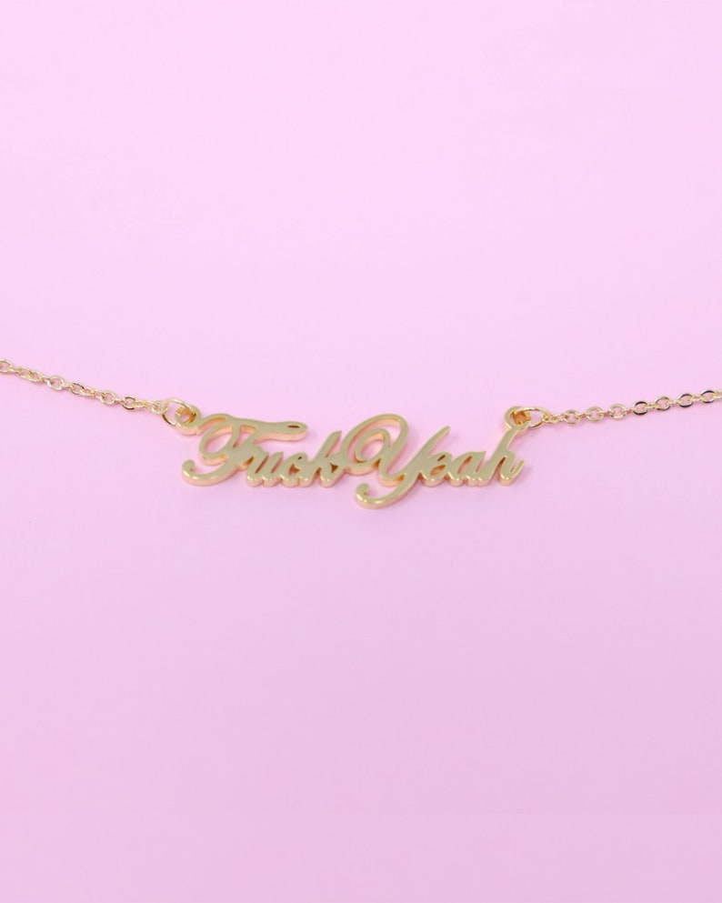 May include: Gold chain necklace with a cursive pendant that reads "Fuck Yeah".