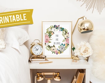 Könnte beinhalten: Druckbarer Wandkunst mit einem Blumenkranz und dem Text "You are so loved". Die Kunst ist in Gold gerahmt und auf einem weißen Nachttisch mit einem goldenen Wecker, einer goldenen Lampe und einer weißen Vase mit weißen Blumen ausgestellt.