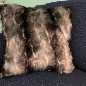 May include: A black and white faux fur throw pillow with a soft, fluffy texture. The pillow is sitting on a dark blue couch.