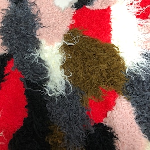 May include: A close-up of a colorful fabric with a fuzzy texture. The fabric is made up of different colored patches, including red, pink, white, brown, black, and gray.