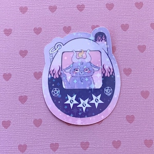 May include: A purple and black digital pet toy sticker with a cartoon demon character inside. The toy has a screen with three stars and the number 6 on each star. The background is a pink pattern of hearts.