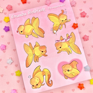 May include: A sheet of stickers featuring illustrations of Oranda goldfish in various poses. The goldfish are yellow with fluffy, white heads and are depicted with different expressions. The stickers are on a pink background with the text "Oranda Goldfish by sugarspice" at the top.