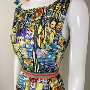 May include: Sleeveless top with a vibrant, artistic print depicting buildings, boats, and figures in blue, yellow, and green hues. The top is accentuated at the waist with a decorative belt. The garment is displayed on a mannequin.