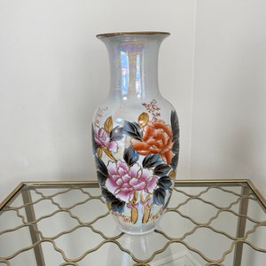 May include: A tall, iridescent white ceramic vase featuring a hand-painted floral design. The vase displays large, detailed pink and orange peony-like flowers with dark blue leaves and gold-toned outlines, finished with a gold-coloured rim.