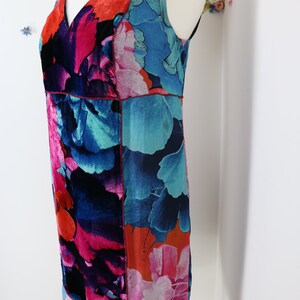 Pode incluir: Vestido sem mangas com estampa floral em tons de azul, rosa e laranja. O vestido apresenta decote em V e silhueta reta. O tecido tem aspecto sedoso e as costuras s&atilde;o acentuadas com pespontos vermelhos. O vestido &eacute; exibido em um manequim.