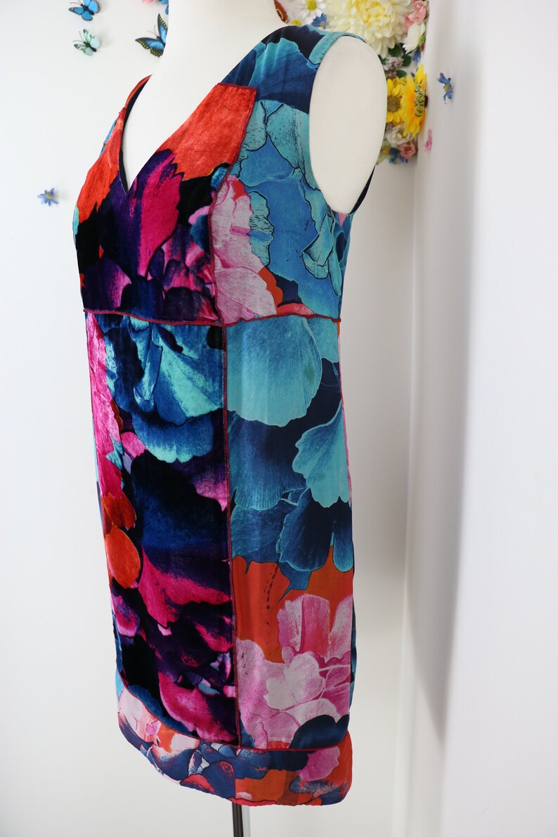 Pode incluir: Vestido sem mangas com estampa floral em tons de azul, rosa e laranja. O vestido apresenta decote em V e silhueta reta. O tecido tem aspecto sedoso e as costuras s&atilde;o acentuadas com pespontos vermelhos. O vestido &eacute; exibido em um manequim.