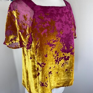 May include: A short-sleeved top featuring a square neckline and a vibrant magenta base color. The garment is adorned with a textured, mustard-yellow velvet floral pattern that covers the lower portion and extends upward in an organic, asymmetrical design.