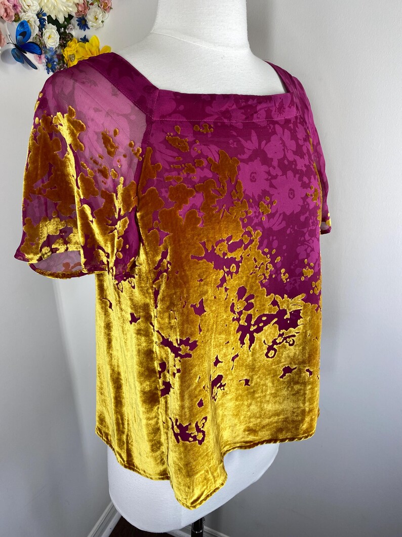 May include: A short-sleeved top featuring a square neckline and a vibrant magenta base color. The garment is adorned with a textured, mustard-yellow velvet floral pattern that covers the lower portion and extends upward in an organic, asymmetrical design.