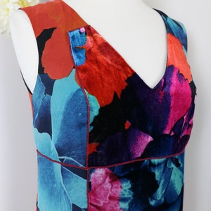Pode incluir: Vestido sem mangas com decote em V, apresentando um vibrante padr&atilde;o floral em tons de azul, vermelho e rosa. O vestido &eacute; exibido em um manequim, mostrando seu design e paleta de cores. O tecido parece ter uma textura aveludada.