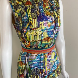 May include: Sleeveless top with a vibrant cityscape print. The design features buildings, water, and boats in shades of yellow, blue, and green. A decorative belt with orange and green accents cinches the waist.
