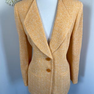 May include: A light orange blazer with a textured fabric. The blazer has a notched collar, two brown buttons, and two front pockets. The jacket is displayed on a mannequin.