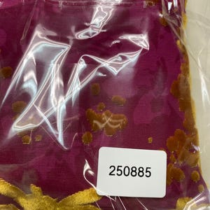 May include: A magenta fabric featuring a raised, textured floral pattern in a golden-brown velvet material. The fabric is encased in a clear plastic protective sleeve with a white rectangular sticker attached, displaying the black printed number 250885.